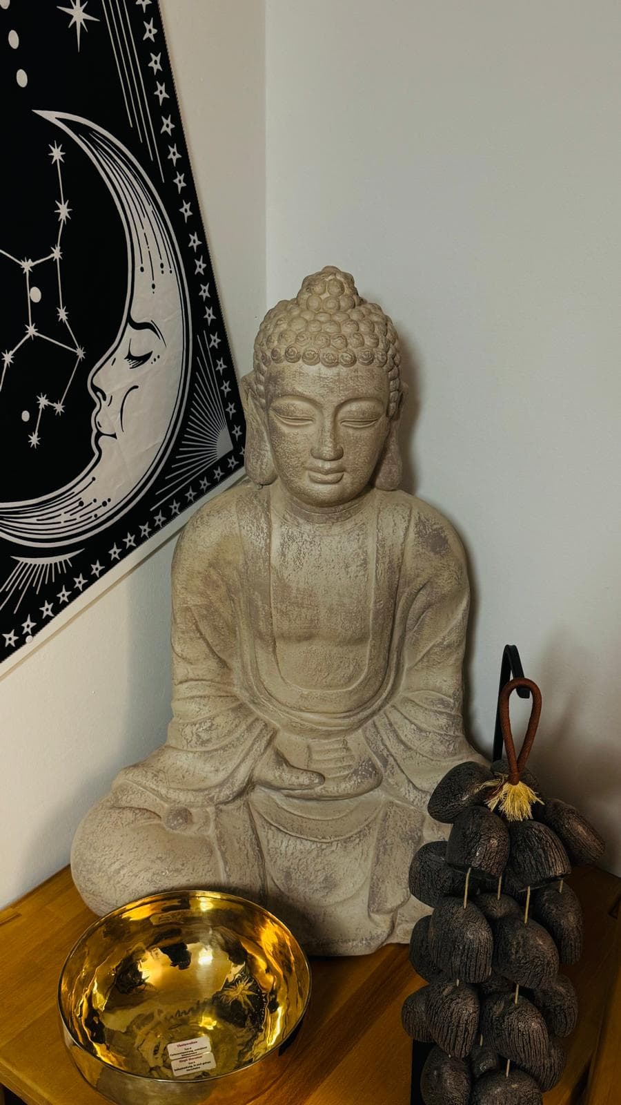 Buddha-Figur mit goldener Klangschale vor dem Mondphasen-Wandbild