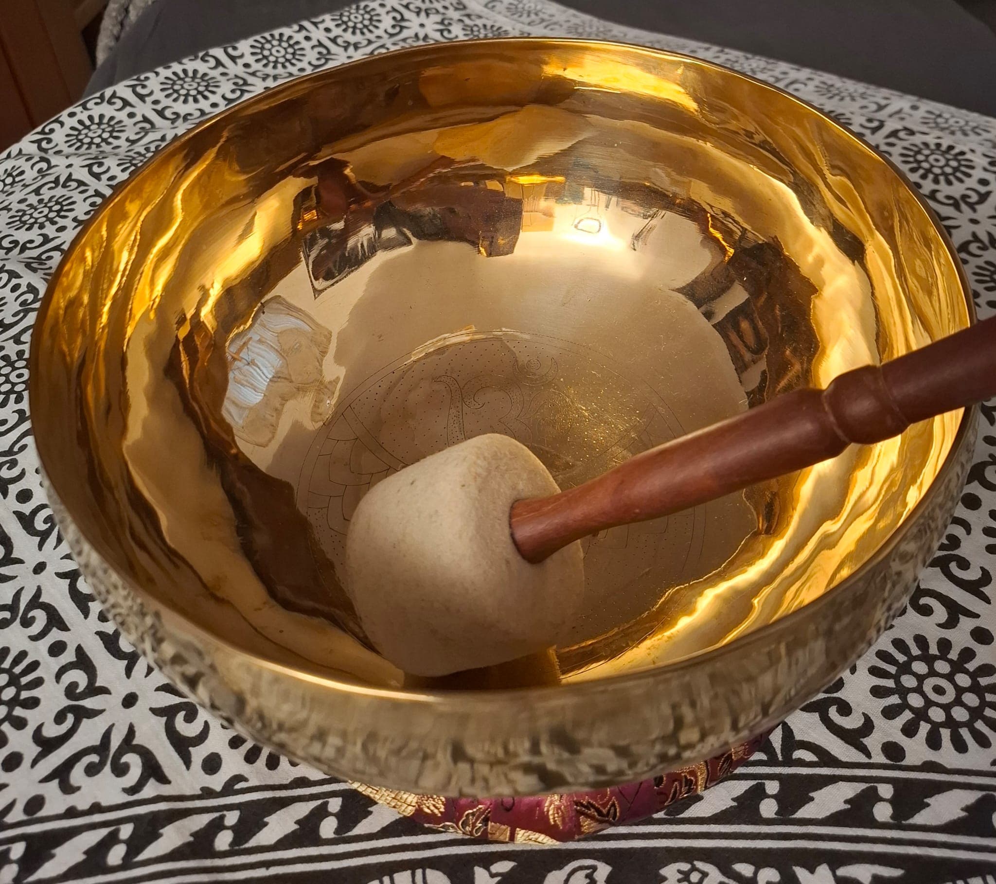 Goldene Klangschale mit Klöppel auf gemustertem Tuch im Klangraum von Marion Gebhardt